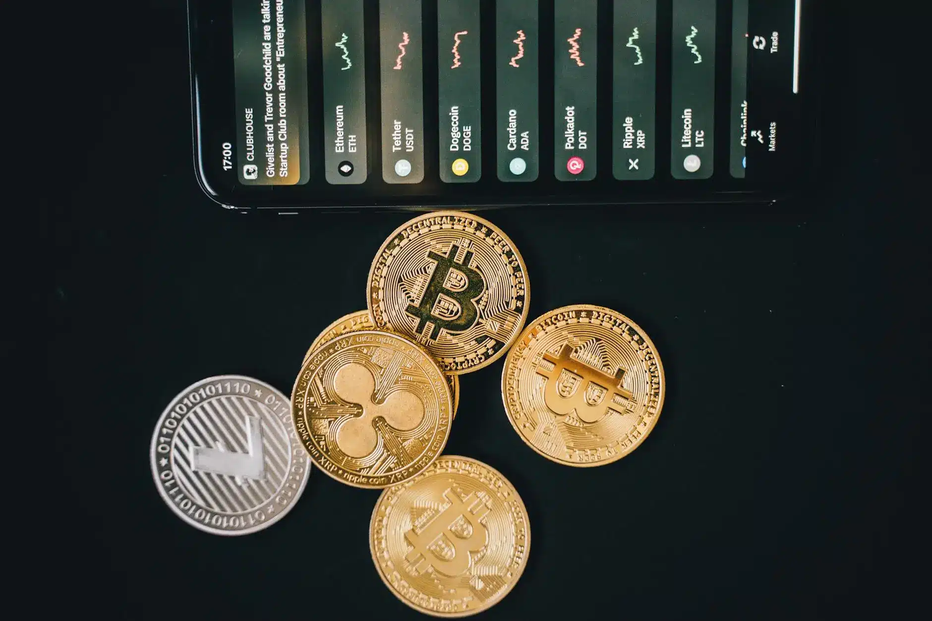 Various cryptocurrency coins including Bitcoin and Ripple, with a smartphone displaying market data.