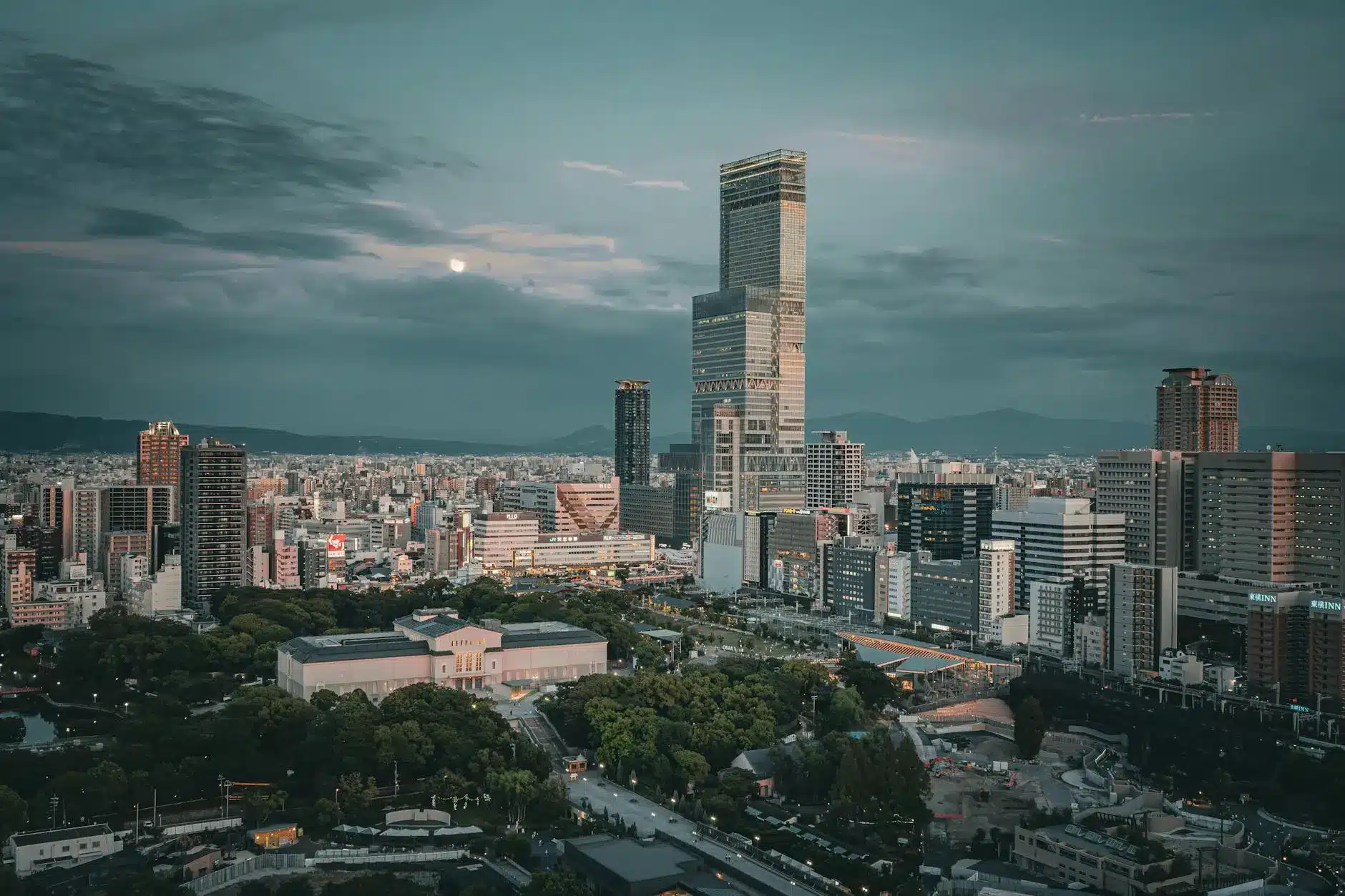 Aerial view of a modern Japanese city skyline with a mix of skyscrapers and greenery.