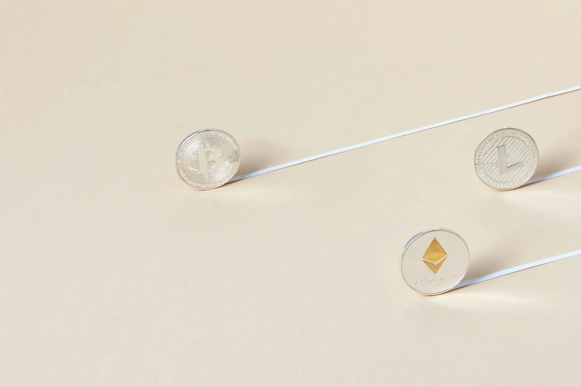 Different cryptocurrency coins including Bitcoin, Litecoin, and Ethereum on a beige background.