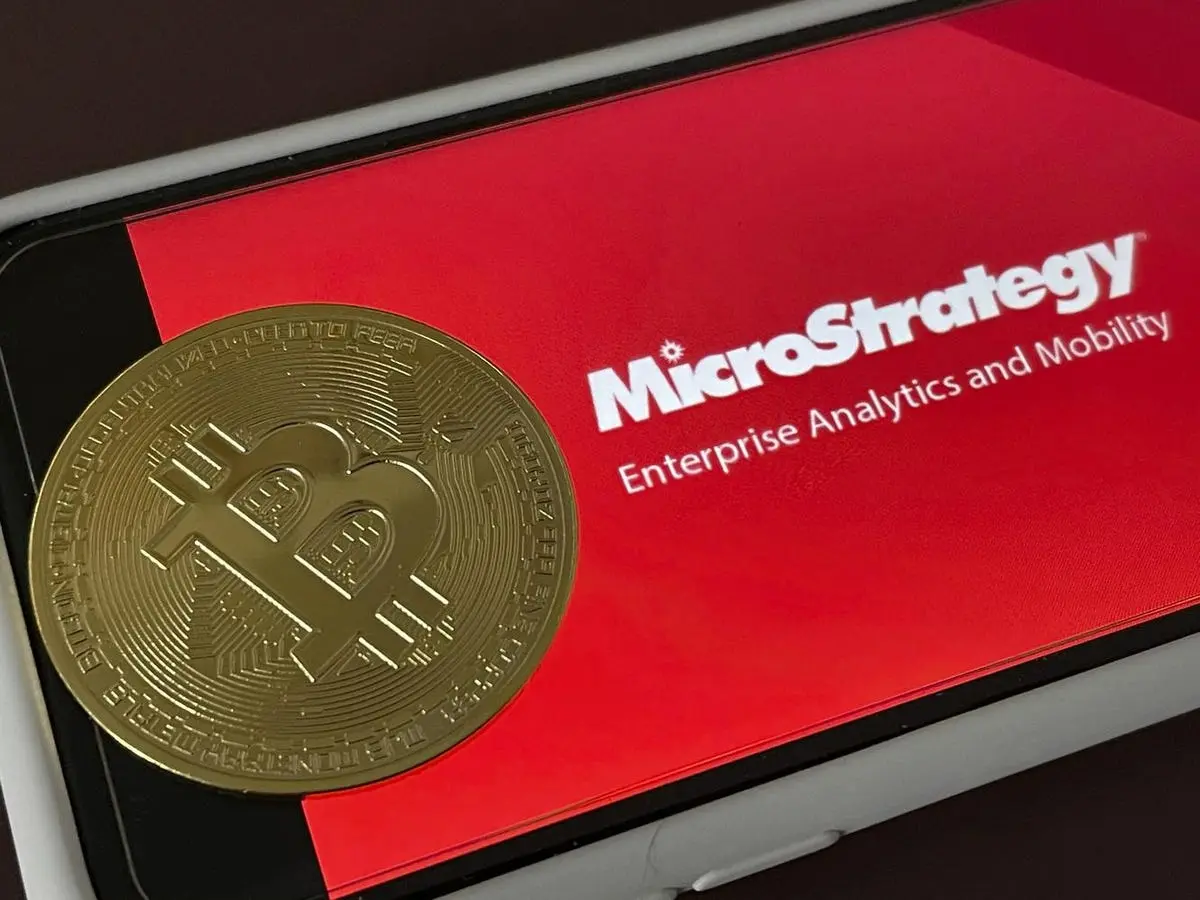 A gold Bitcoin on a smartphone screen displaying MicroStrategy logo and text.