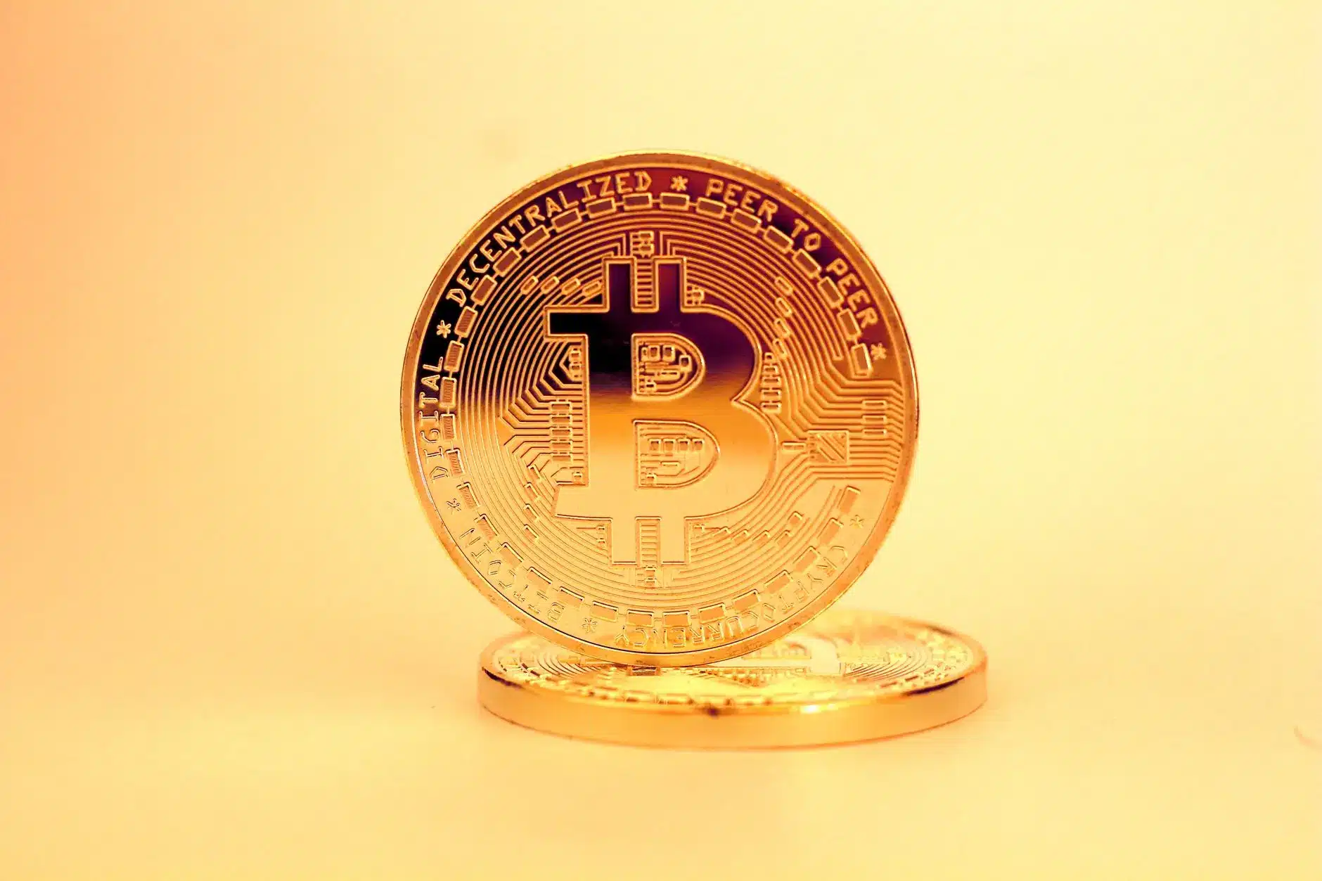 Close-up of gold Bitcoin coins on a gradient background.