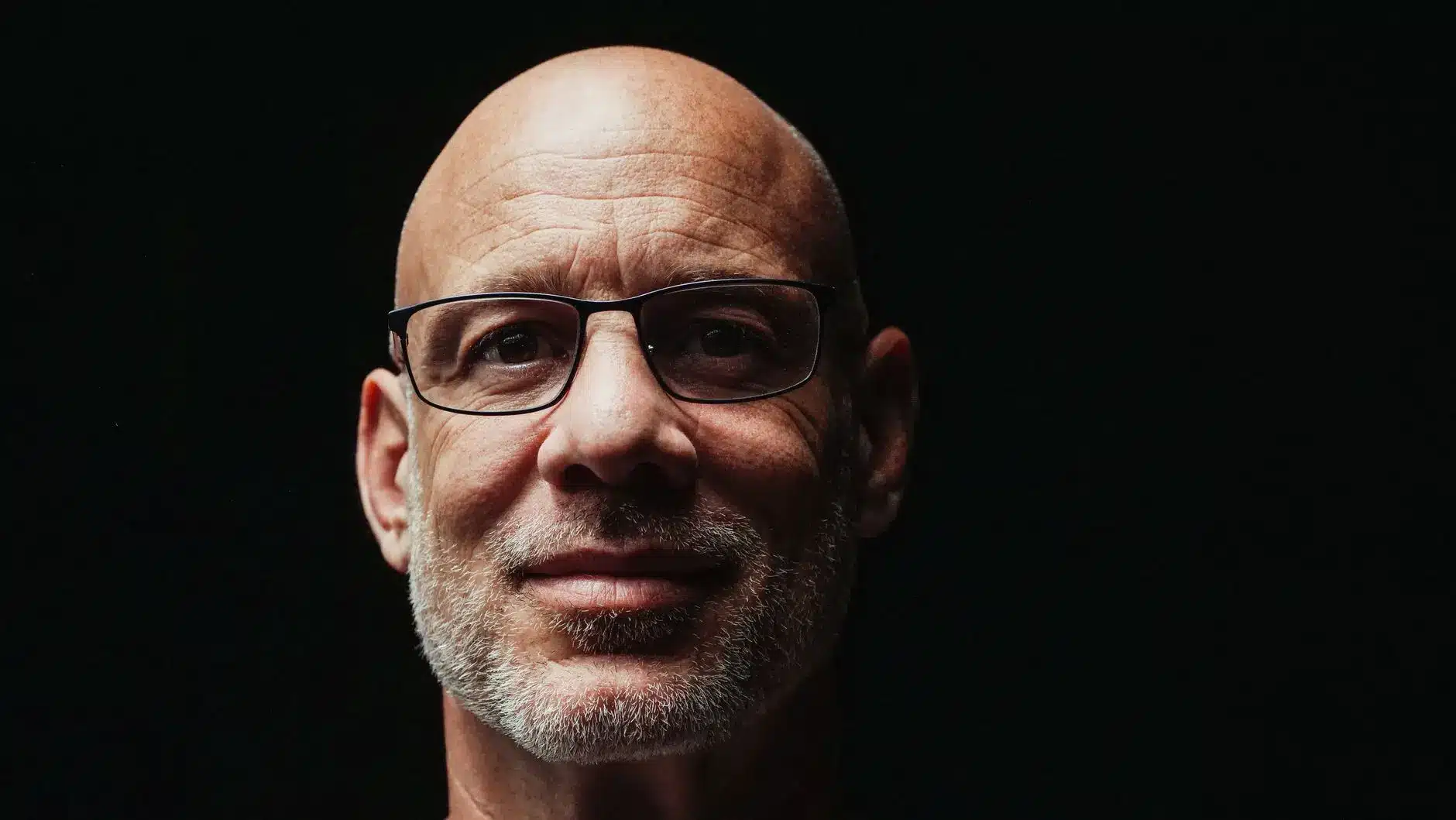 Close-up portrait of Adam Aron, CEO of AMC Entertainment, wearing glasses against a black background