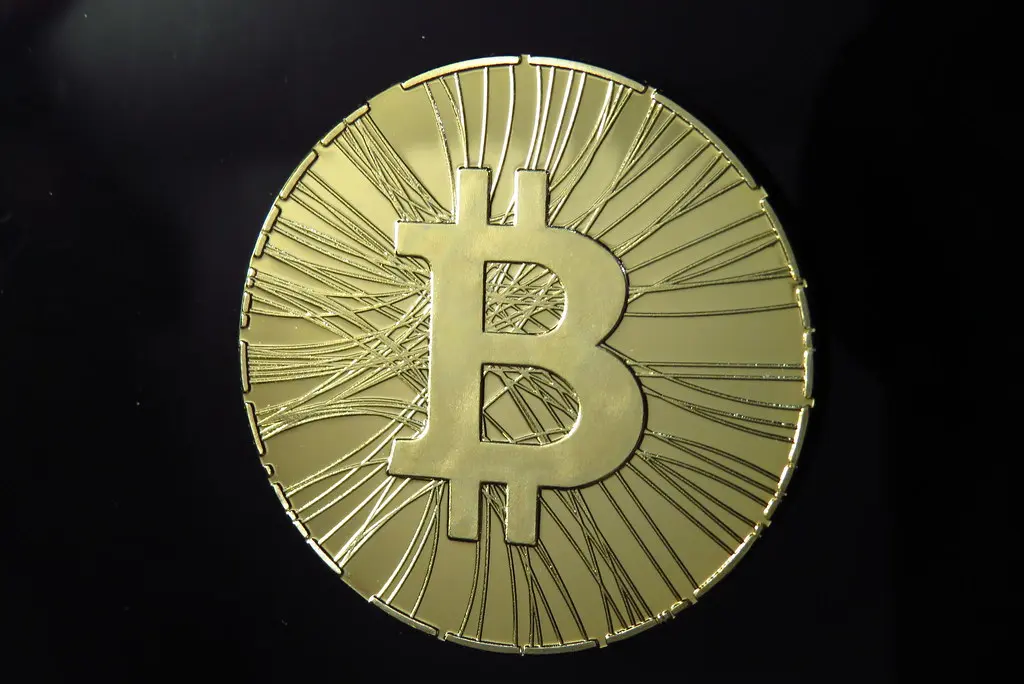 Eine goldfarbene physische Münze mit dem Bitcoin-Logo vor einem schwarzen Hintergrund.