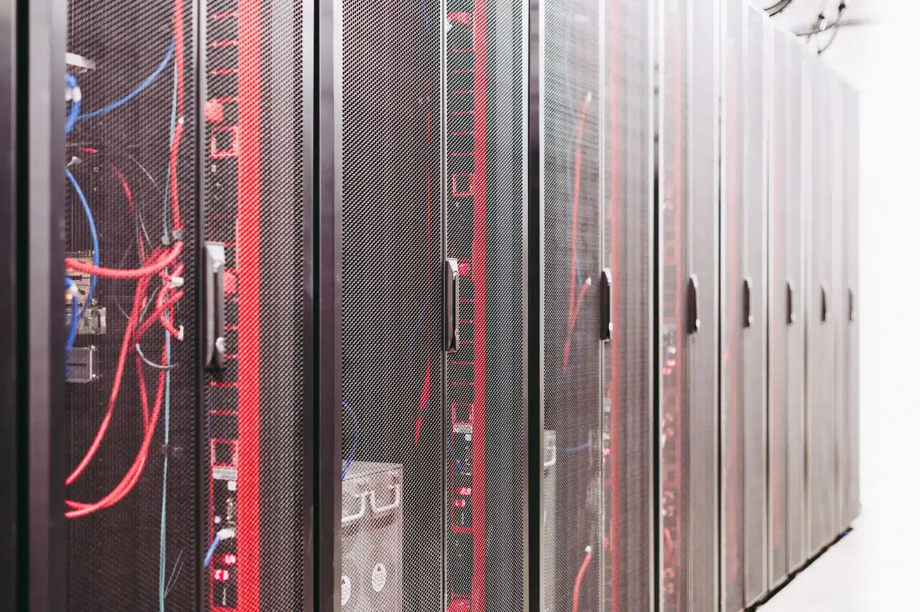 Row of black mesh server racks in a datacenter with visible red and blue network cabling
