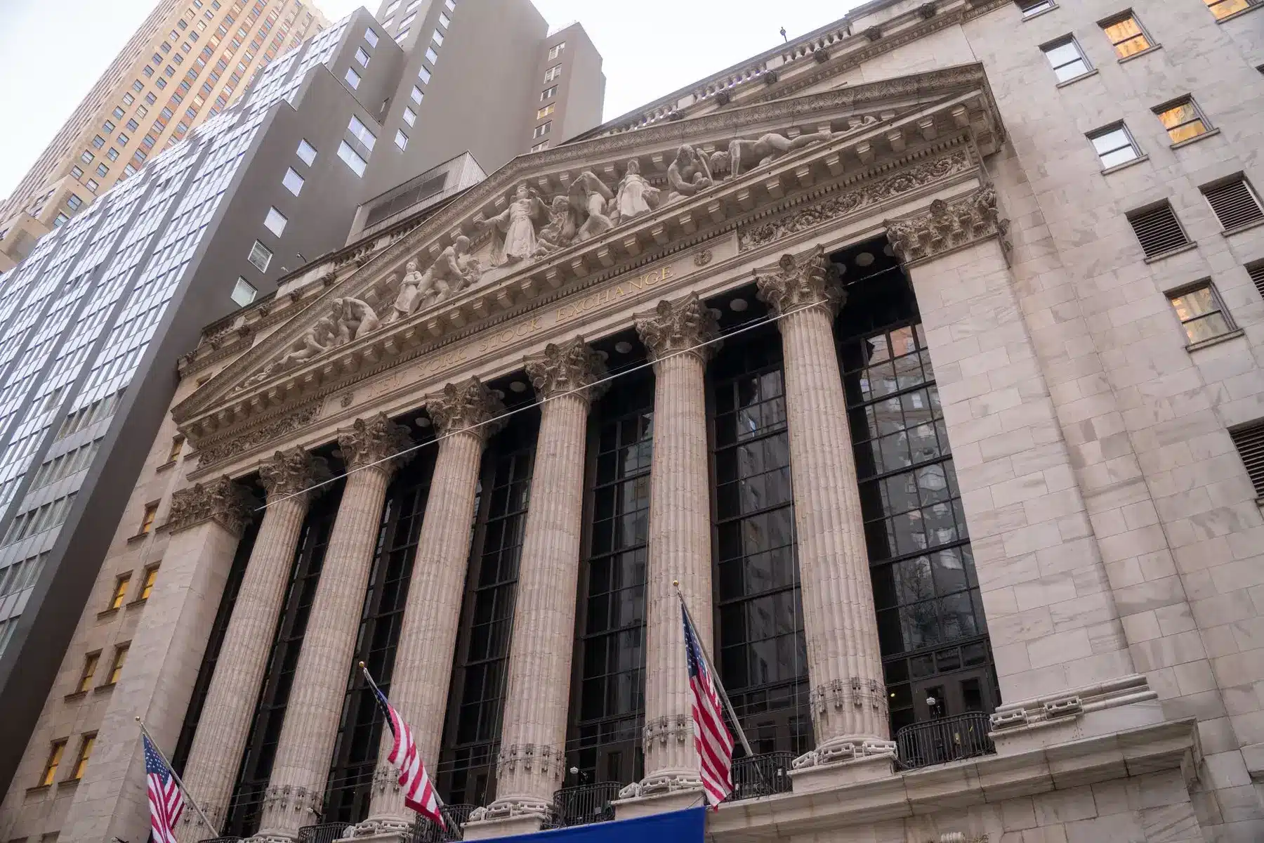 Low angle view of the New York Stock Exchange building facade with Corinthian columns and American flags