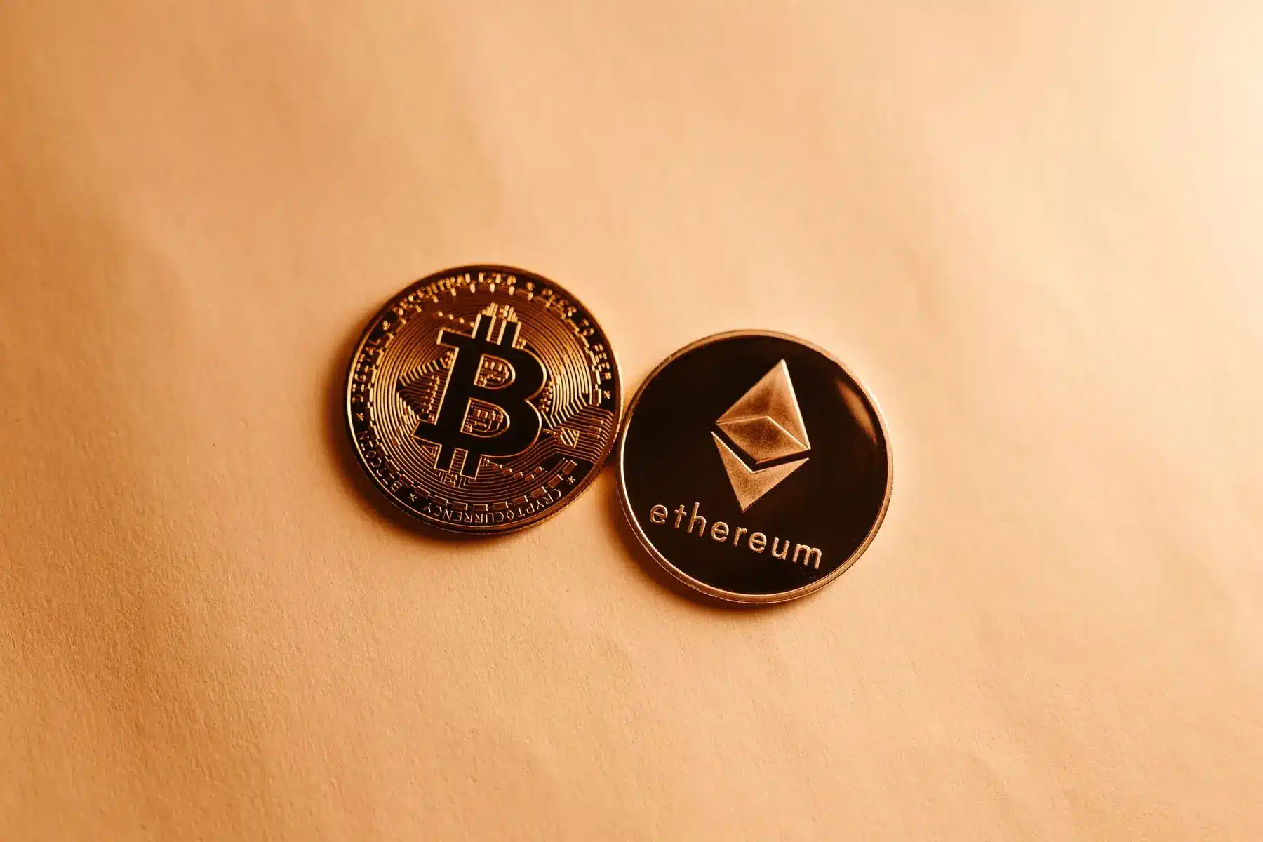 Physical gold Bitcoin and black Ethereum tokens resting on a light-colored surface.