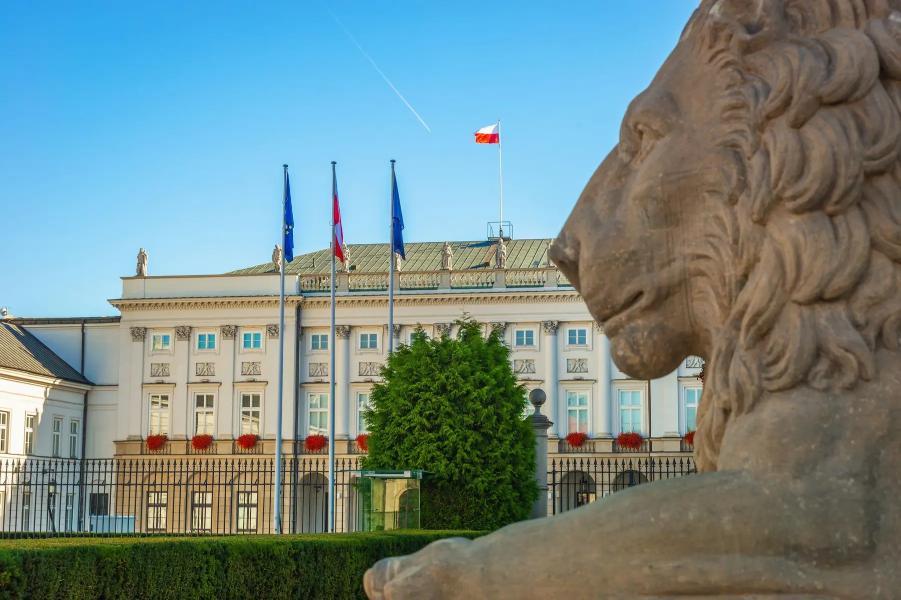 The Sejm building in Warsaw with the Polish flag flying on top and a lion statue in the foreground