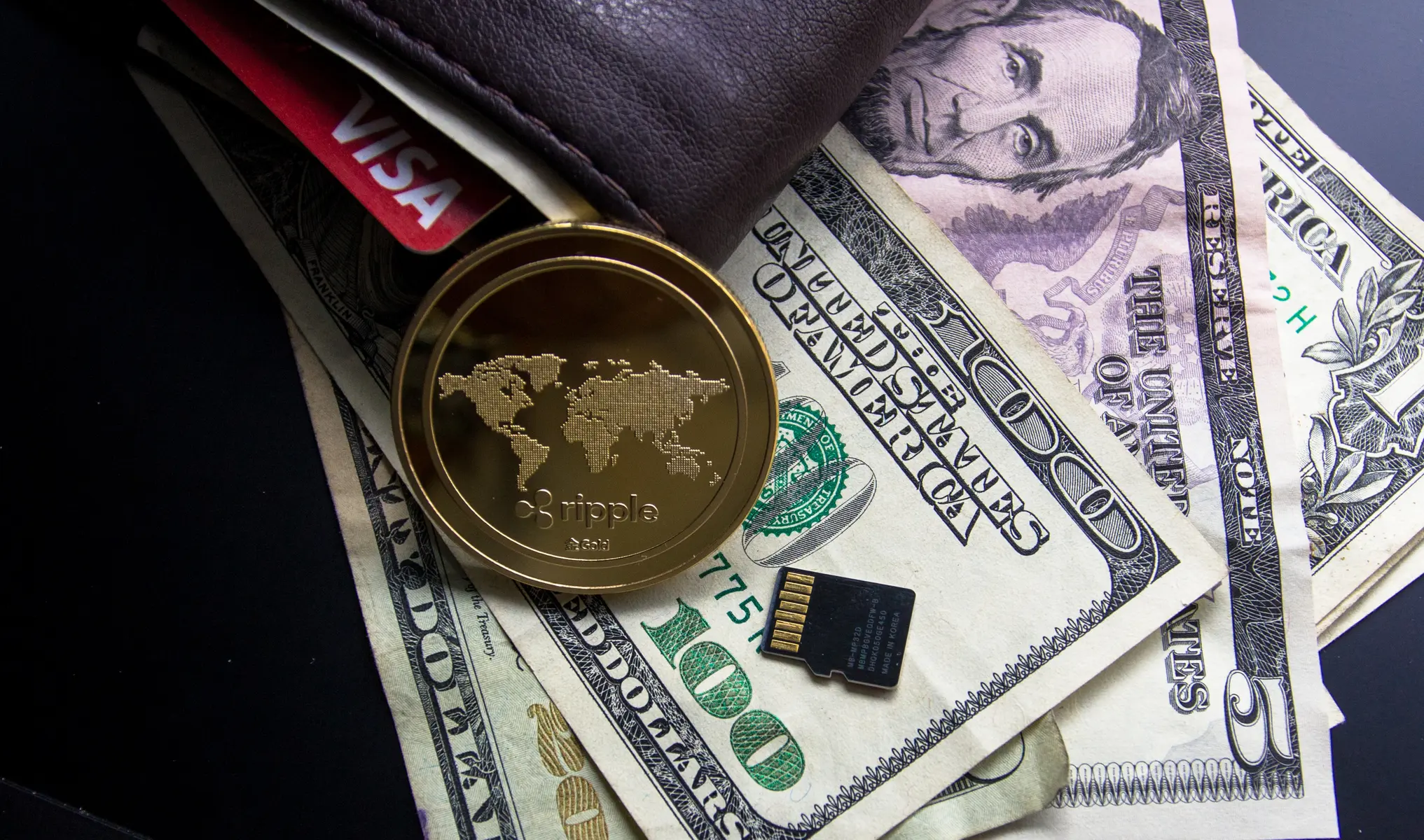 Eine goldene Ripple XRP Münze auf US-Dollar-Banknoten neben einer Brieftasche und einer microSD-Karte.