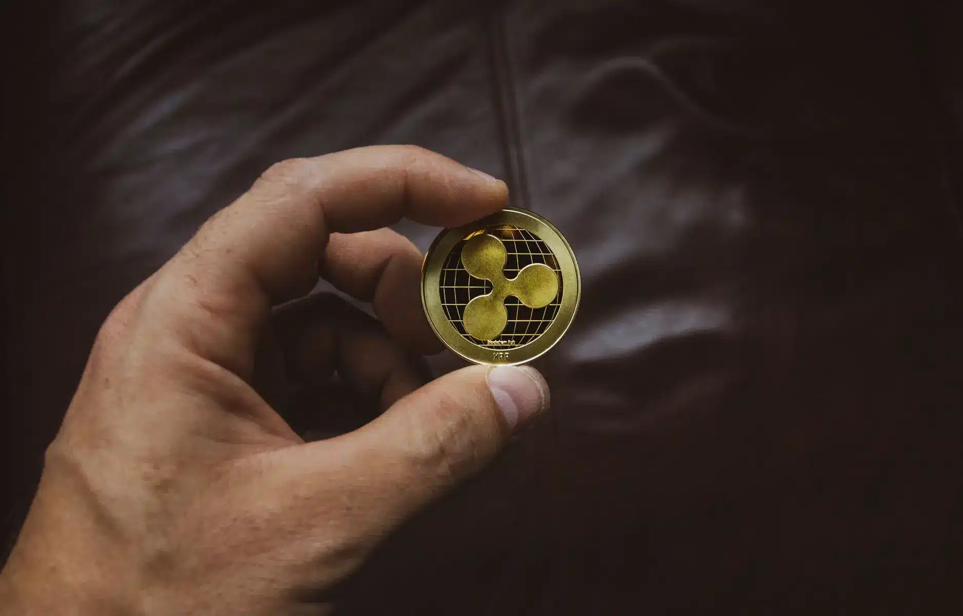 A person holding a physical gold-colored XRP cryptocurrency coin between their fingers.