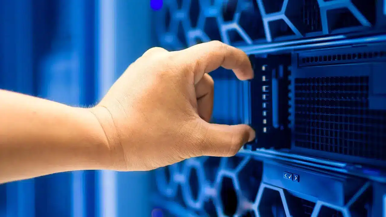 Eine Hand, die ein Modul in einem blau beleuchteten Serverrack eines Rechenzentrums bedient.