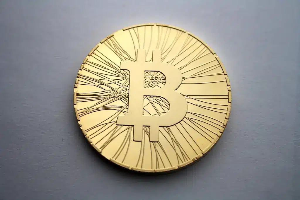 Eine goldfarbene physische Bitcoin-Münze mit dem charakteristischen B-Symbol auf grauem Hintergrund.