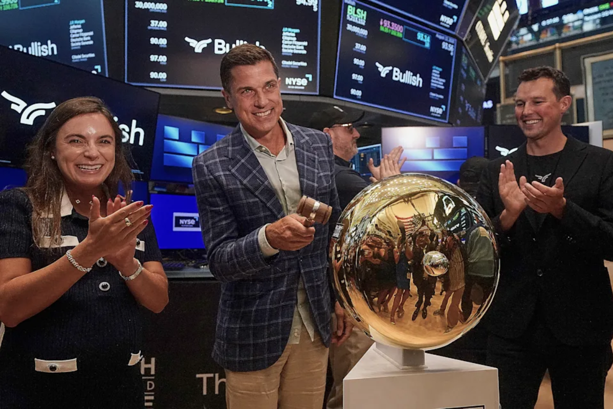 Bullish CEO Tom Farley, center, is flanked by Coin Desk CEO Sara Stratiberdha, and Bullish Chairman Brendan Blumer, as he rings the ceremonial bell of the New York Stock Exchange. (AP Photo/Richard Drew) · ASSOCIATED PRESS
