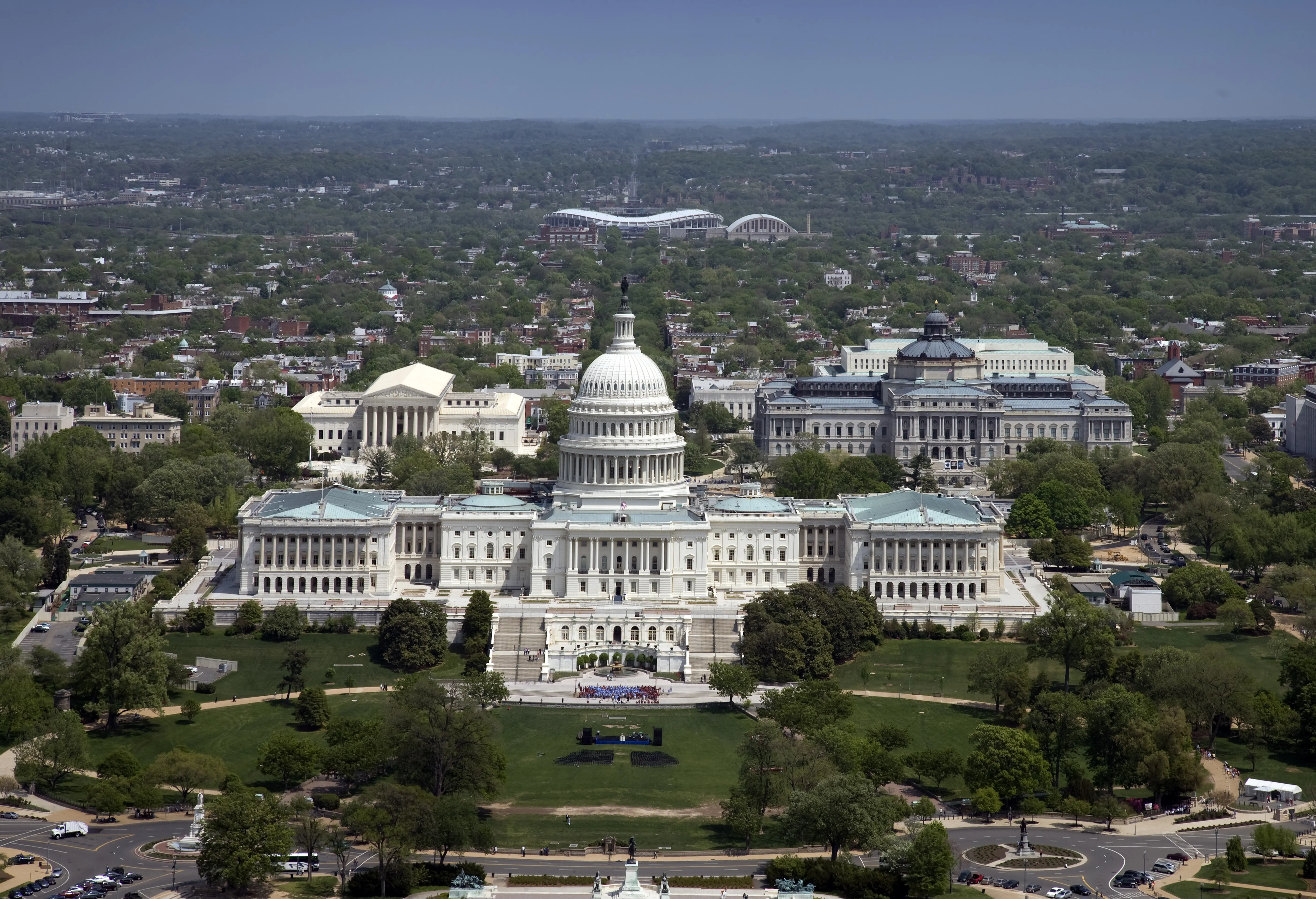 Aerial view of the US Capitol Building surrounded by green trees and cityscape.
