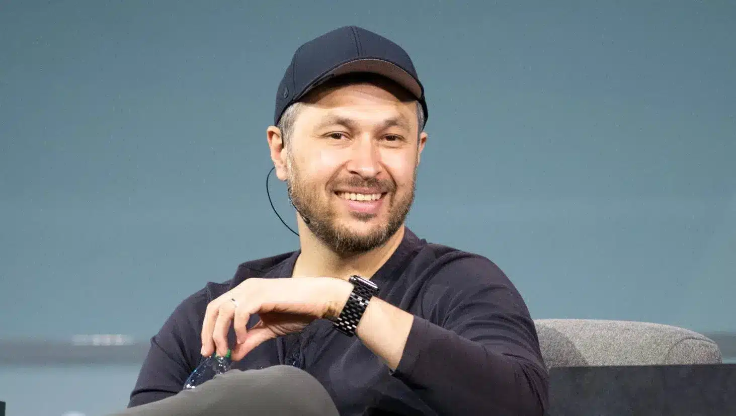 Anatoly Yakovenko wearing a black baseball cap and black shirt, smiling during a speaking engagement.